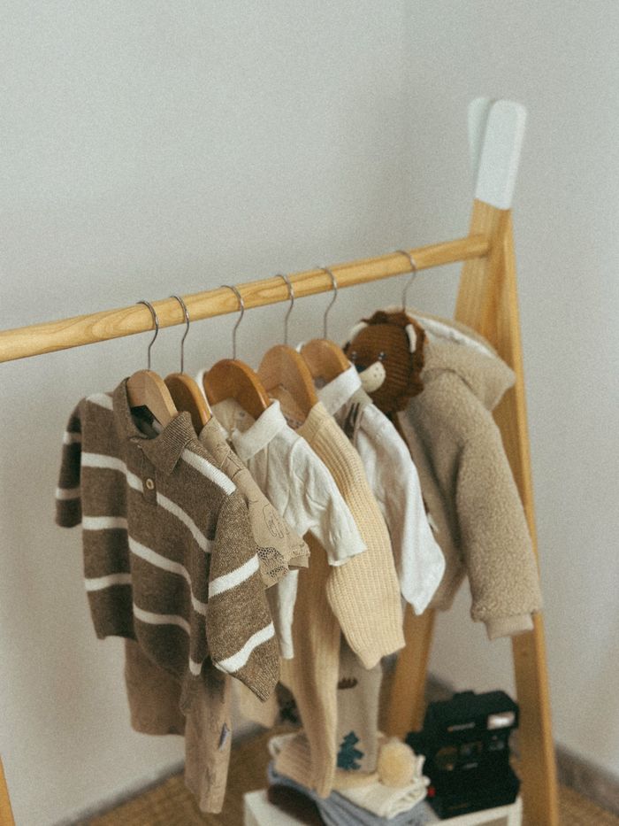 Warm neutral-toned baby clothes hanging on a wooden rack in a nursery.