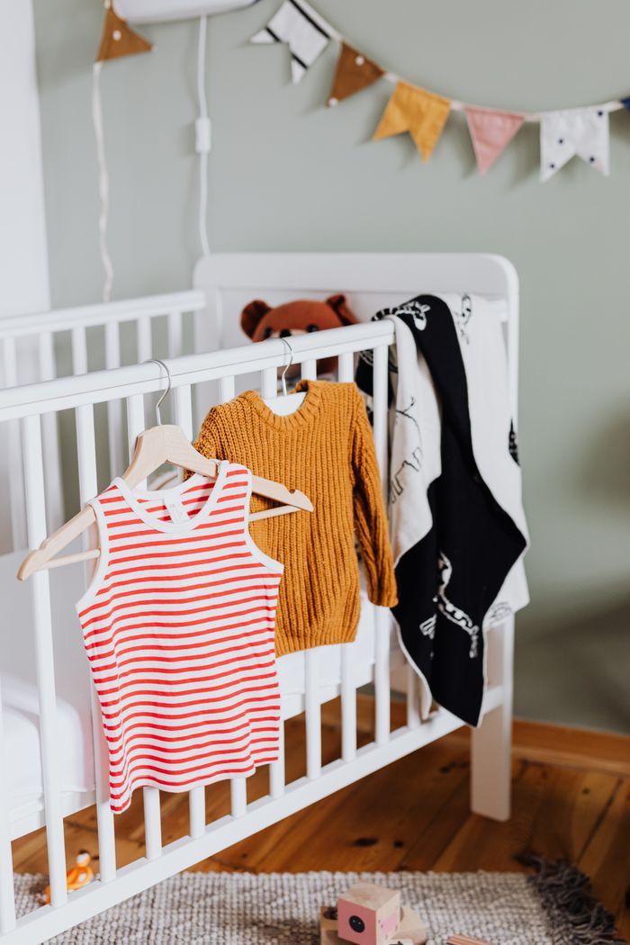 A warm baby room with a crib, clothes, and playful decorations.